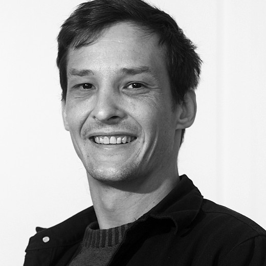 Black and white portrait of James Wilson, smiling, in a dark jacket over a knitted jumper